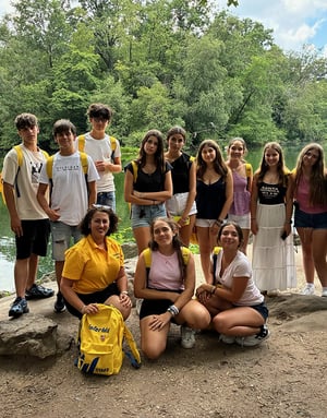 Un grupo de alumnos de InterWay posa en una orilla rocosa rodeada de frondosa vegetación verde durante una excursión a un entorno natural en Maryland.