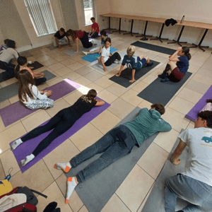 Un grupo de estudiantes realiza ejercicios de estiramiento y yoga sobre esterillas en una sala interior durante el campamento multiactividad de InterWay en Irlanda.