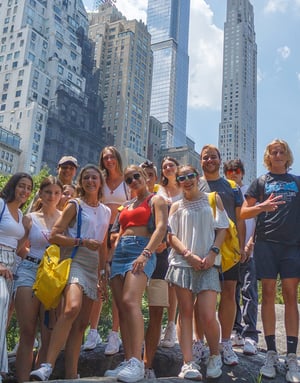 Grupo de jóvenes estudiantes de InterWay con mochilas amarillas posando juntos en una avenida de Nueva York rodeados de los grandes rascacielos de Manhattan.