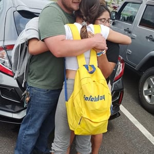 Un emotivo abrazo de despedida o bienvenida entre una estudiante con mochila amarilla de InterWay y un miembro de su familia de acogida en Estados Unidos.