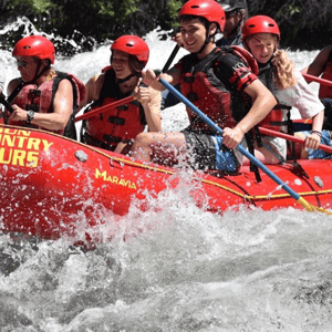 Estudiantes de un curso de inglés en Oregón haciendo rafting en un río de aguas bravas, equipados con chalecos salvavidas y cascos rojos.