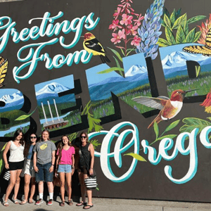 Alumnas del programa de idiomas de InterWay posando frente a un mural colorido que dice 