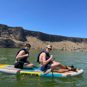 Dos estudiantes del viaje de idiomas de InterWay en Oregón practicando paddle surf en un entorno natural con cañones rocosos al fondo.