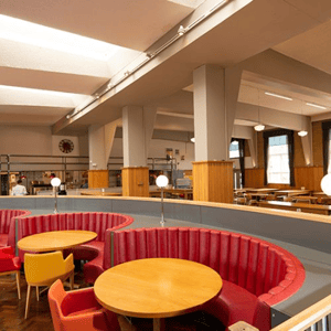 Comedor moderno con mesas redondas de madera y sofás semicirculares rojos en las instalaciones de Oxford Brookes University, preparado para los estudiantes de InterWay.