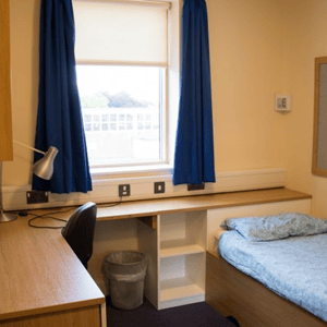 Habitación individual con escritorio de madera, ventana con cortinas azules y cama en la residencia de Oxford Brookes University para los alumnos de InterWay.