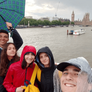 Alumnos del curso de Oxford de InterWay sonriendo con paraguas y chubasqueros junto al río Támesis durante su excursión de un día a Londres.
