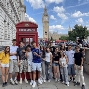 Grupo de estudiantes del programa de idiomas de InterWay posando junto a una cabina telefónica roja tradicional durante su excursión a Londres desde Oxford.