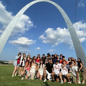 Gran grupo de estudiantes del viaje de idiomas de InterWay alineados para una foto de recuerdo sobre el césped frente al monumental arco Gateway Arch en St. Louis.