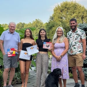 Un grupo de alumnos de InterWay y miembros de su familia de acogida posan sonrientes en un jardín exterior junto a un perro negro en Seattle.