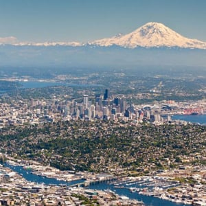 Impresionante vista aérea de la ciudad de Seattle rodeada de agua y vegetación, con el Monte Rainier nevado destacando al fondo, actividad del curso de InterWay.