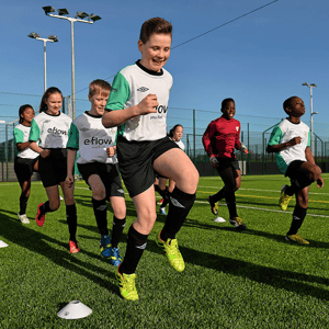Grupo de niños y niñas corre entusiasmado sobre el césped artificial durante un entrenamiento de fútbol del Soccer Camp de InterWay en Irlanda.