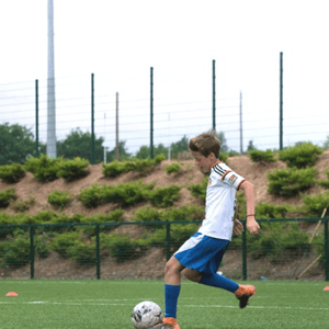 Un alumno del campus de fútbol de InterWay en Irlanda concentrado mientras controla y chuta un balón en un campo deportivo al aire libre.