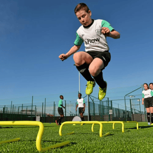 Un joven futbolista realiza saltos de potencia sobre vallas de entrenamiento amarillas durante el Soccer Camp residencial de InterWay en Irlanda.