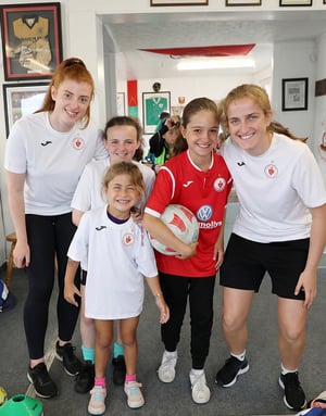 Un grupo de cinco jugadoras y entrenadoras sonriendo juntas en el interior del club del Soccer Camp de InterWay en Irlanda, con una de las niñas sosteniendo un balón de fútbol.