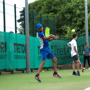 Un estudiante del curso de tenis e idiomas de InterWay en Irlanda realiza un golpe de derecha en una pista exterior con lonas verdes de fondo.