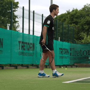 Un jugador caminando con la raqueta en la mano por la línea de fondo de una pista de tenis durante las sesiones de entrenamiento del campus de InterWay.