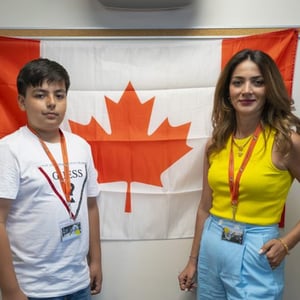 Un alumno y una alumna del programa de idiomas de InterWay posan sonrientes a ambos lados de una gran bandera de Canadá colgada en la pared.
