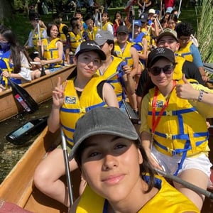 Grupo de estudiantes del campamento de InterWay sentados y sonriendo a bordo de un barco turístico equipados con chalecos salvavidas amarillos.