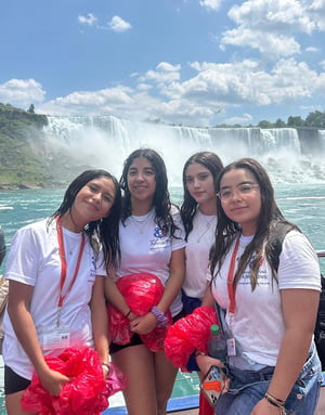 Cuatro estudiantes del viaje de idiomas de InterWay posan juntas vistiendo camisetas blancas durante una excursión a las impresionantes Cataratas del Niágara en Canadá.