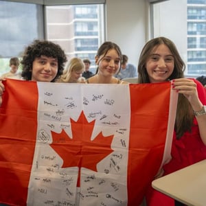Tres estudiantes del curso de InterWay en Toronto posan sonrientes en el aula sosteniendo una gran bandera de Canadá.