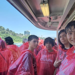 Estudiantes del programa de idiomas de InterWay protegidos con chubasqueros rojos a bordo de un barco turístico durante una excursión acuática en Canadá.