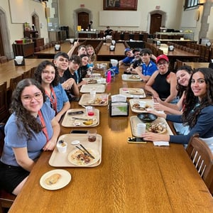 Alumnos del viaje de verano de InterWay sentados alrededor de una gran mesa de madera compartiendo una comida en el comedor del campus en Toronto.