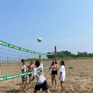 Estudiantes del campamento de InterWay jugando un partido de voleibol en una pista de arena al aire libre en un día despejado.