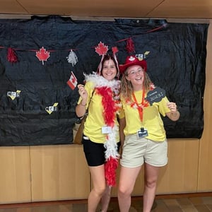 Dos jóvenes estudiantes de InterWay con camisetas amarillas posan sonrientes en una sala interior decorada para una actividad festiva en Canadá.