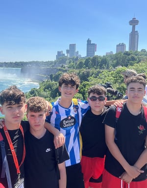 Cinco jóvenes alumnos del curso de inglés de InterWay posan juntos al aire libre con un frondoso paisaje verde, el mar y los rascacielos de la ciudad al fondo.