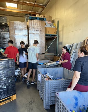 Jóvenes voluntarios del programa de InterWay en Estados Unidos trabajando en un banco de alimentos y clasificando productos en grandes contenedores dentro de un almacén.