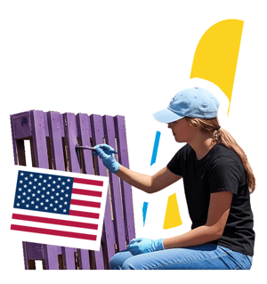 Voluntaria pintando madera reciclada para el programa de InterWay en Estados Unidos, integrado con la bandera estadounidense y gráficos amarillos.