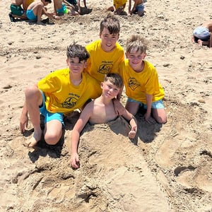 Grupo de niños con camisetas amarillas jugando en la arena de la playa durante una excursión de campamento internacional de interway