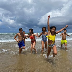 Grupo de niños corriendo en la orilla del mar bajo un cielo nublado disfrutando de un viaje de inmersión en la naturaleza con Interway