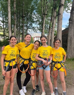 Grupo de niñas con camisetas amarillas equipadas con arneses de seguridad en un bosque listas para hacer tirolina y multiaventura