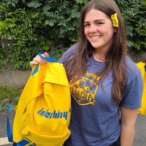 Chica adolescente sonriente sosteniendo una mochila amarilla de Interway en un entorno natural rodeada de vegetación