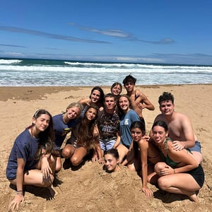 Adolescentes sentados y disfrutando en la arena de la playa en un campamento de verano internacional de Interway
