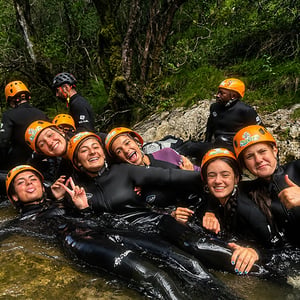 Grupo de jóvenes sonriendo en el agua con trajes de neopreno durante una experiencia de aventura de Interway