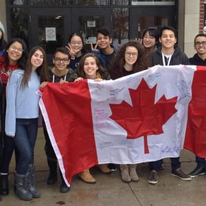 Grupo de alumnos de Interway posando sonrientes tras la bandera de Canadá durante su año escolar